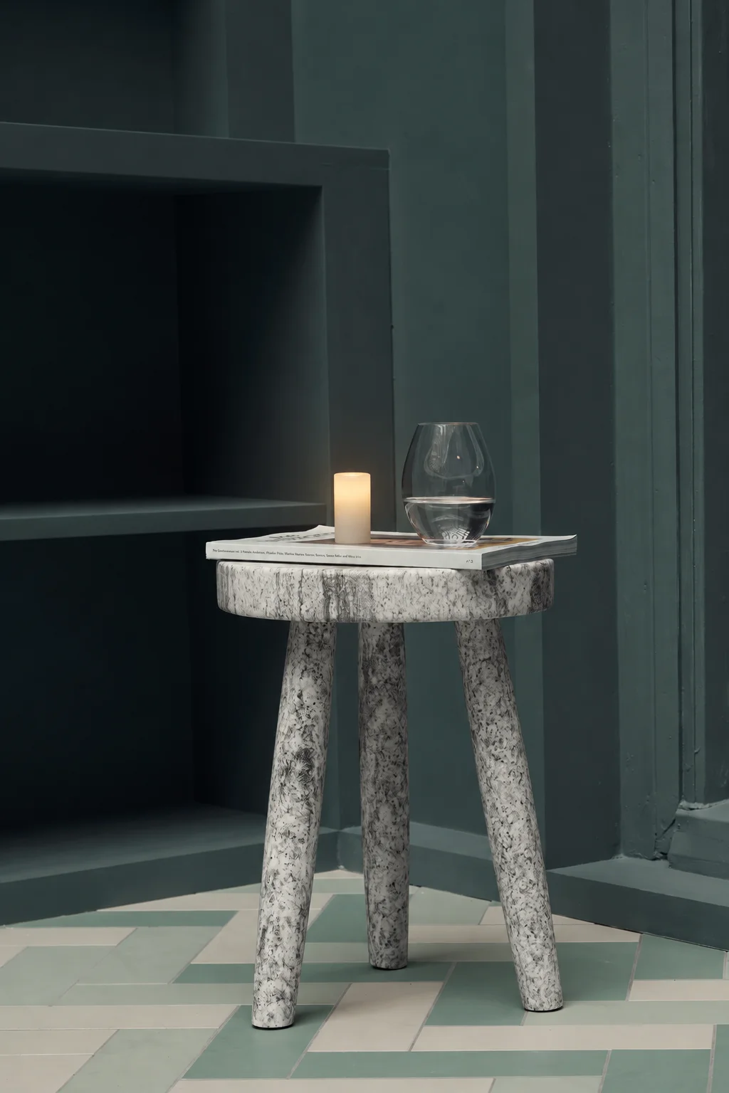 A glowing Context candle on a sculptural stone side table against dark wall panels